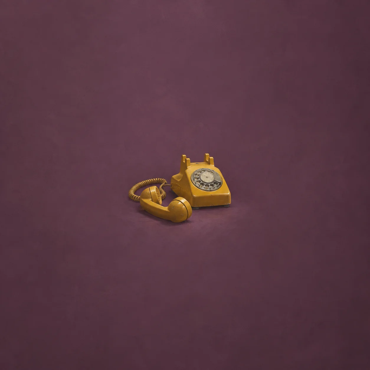 A mustard-yellow rotary telephone with its receiver set beside it on a plum background.