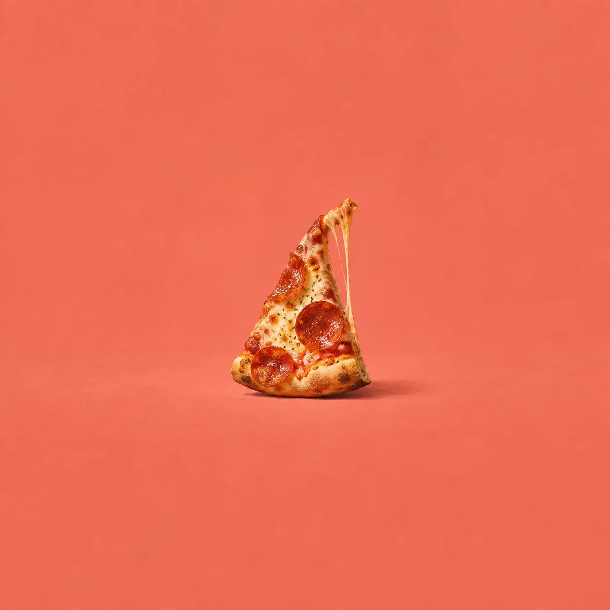 A pepperoni pizza slice stands on its crust with a thin strand of cheese stretching down against coral.