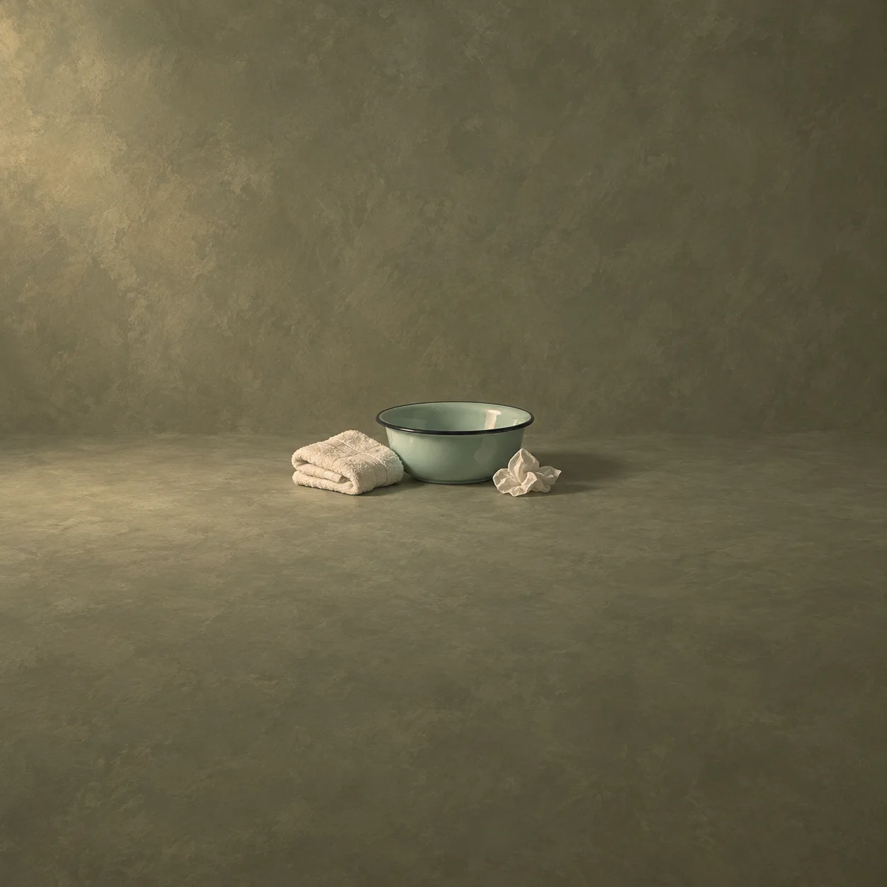 A pale green enamel basin beside a folded towel and a crumpled tissue against an olive-grey background.
