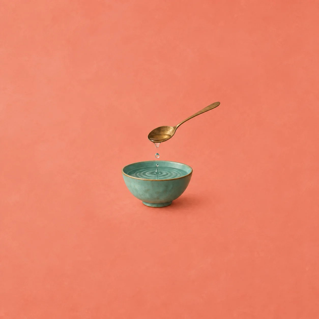 A brass spoon releases a drop into rippling water in a small turquoise bowl against coral.