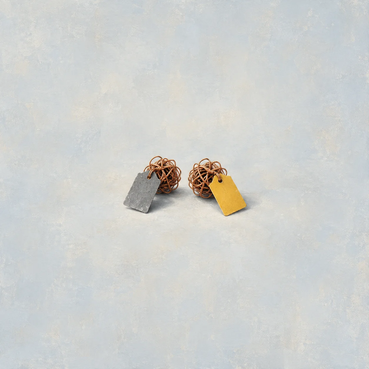 Two tangled copper wire balls, one with a gray tag and the other with a yellow tag, against a pale blue background.