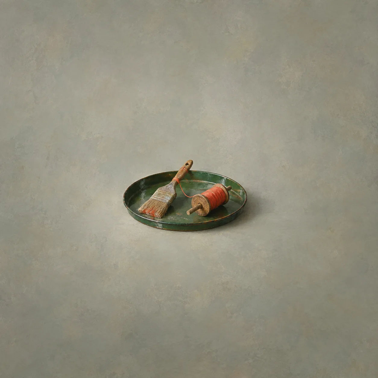 A paintbrush and a wooden spool wound with red thread on a green enamel tray.