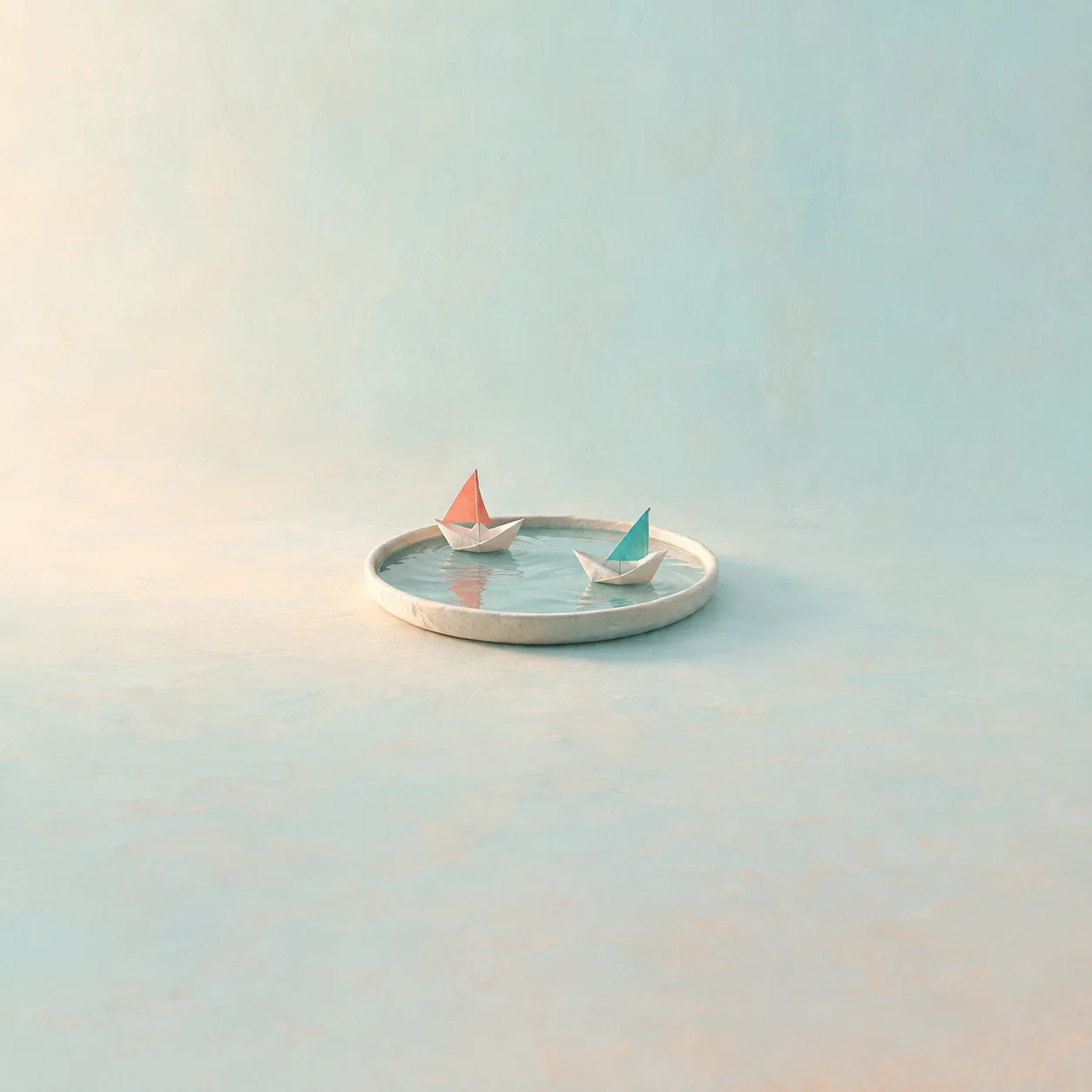 Two small paper boats with coral and teal sails floating on a tray of water.