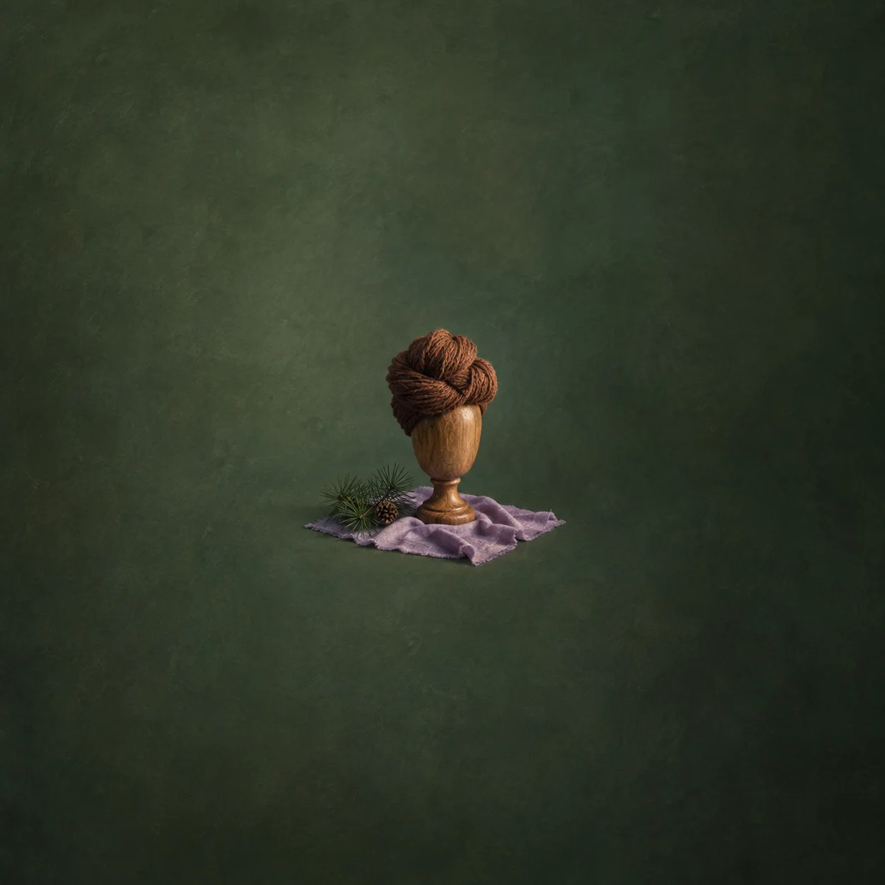 A wooden mannequin head wears a knot of brown yarn above lavender fabric and a small green sprig.