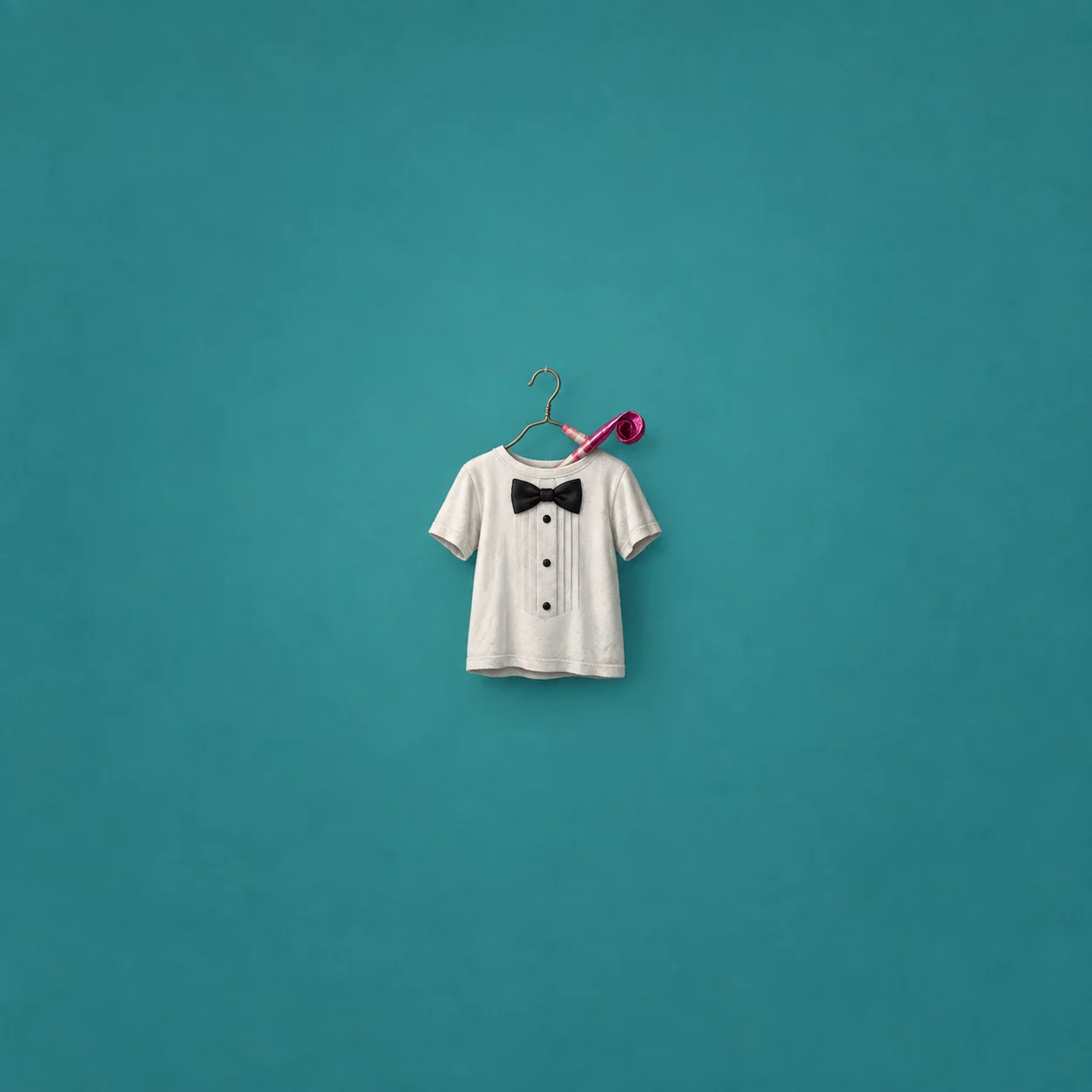 A white T-shirt with a black bow tie and buttons hangs from a wire hanger beside a pink party horn.