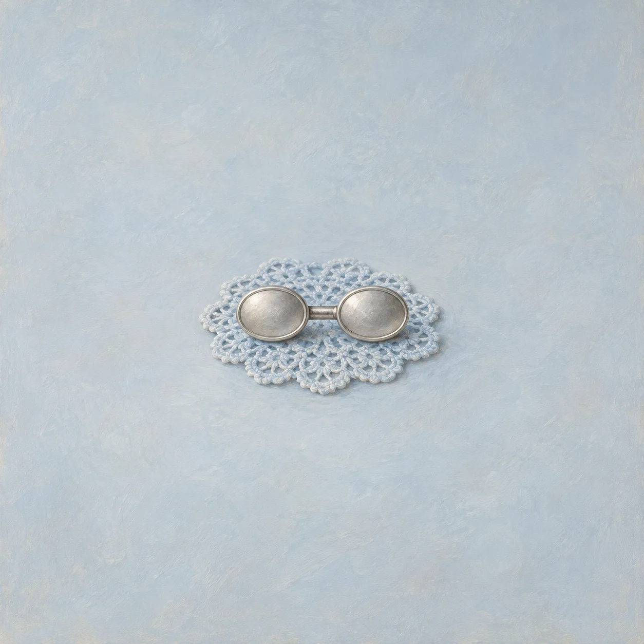 Painterly two round silver discs joined by a short bar on a pale lace doily.