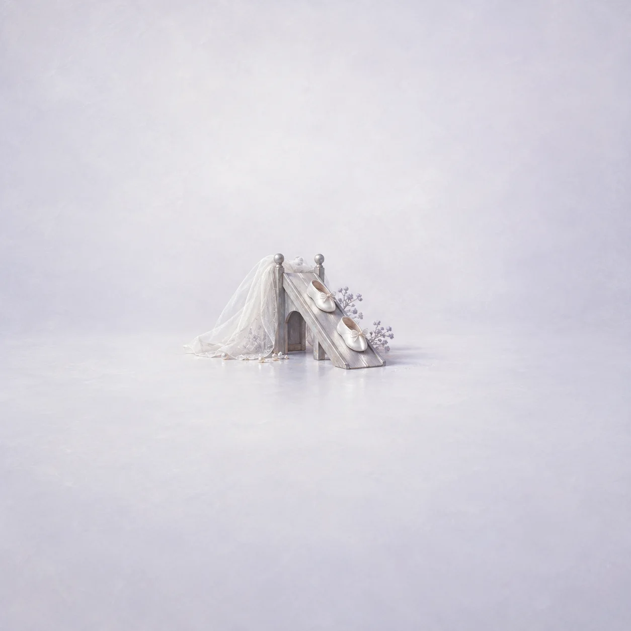 A white veil draped over a tiny ramp with miniature white slippers resting on it.