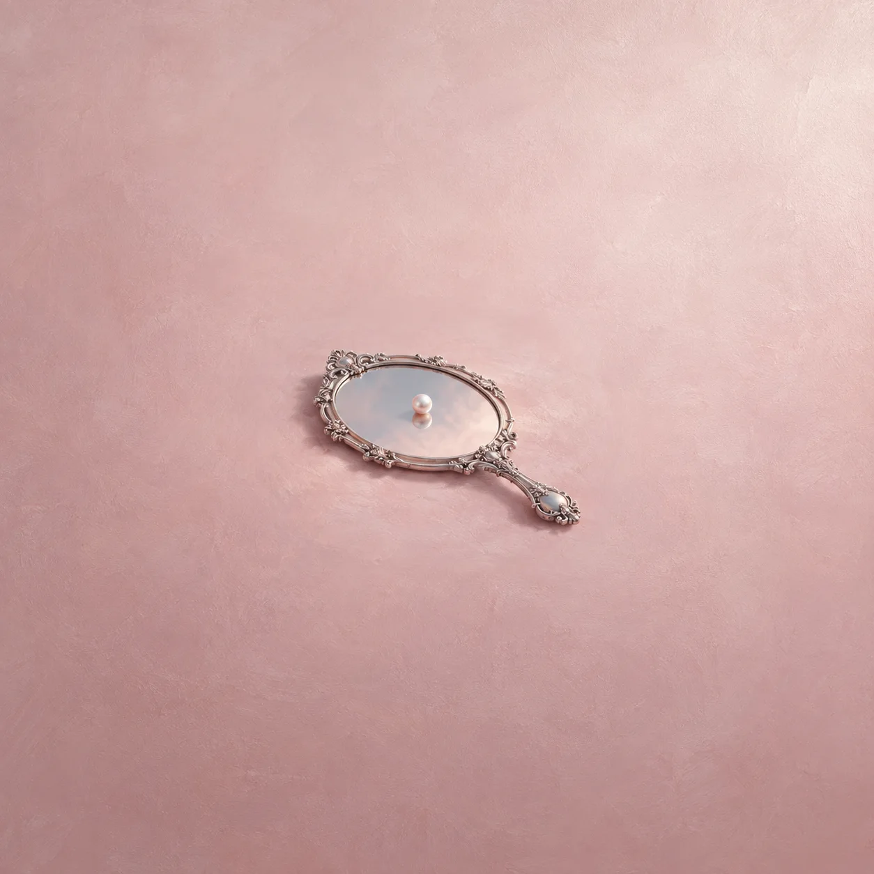 Painterly small pearl resting on an ornate silver hand mirror against pale pink.