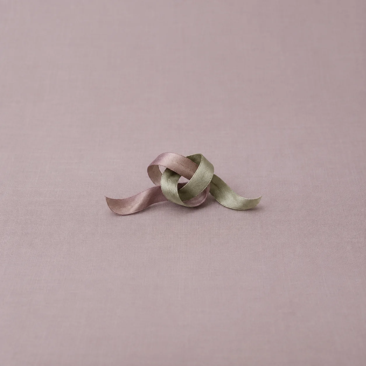 Mauve and sage ribbons loop around one another on pale fabric.