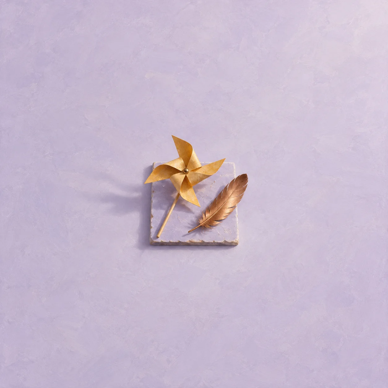 An ochre paper pinwheel and a brown feather rest on a small square of lilac paper.