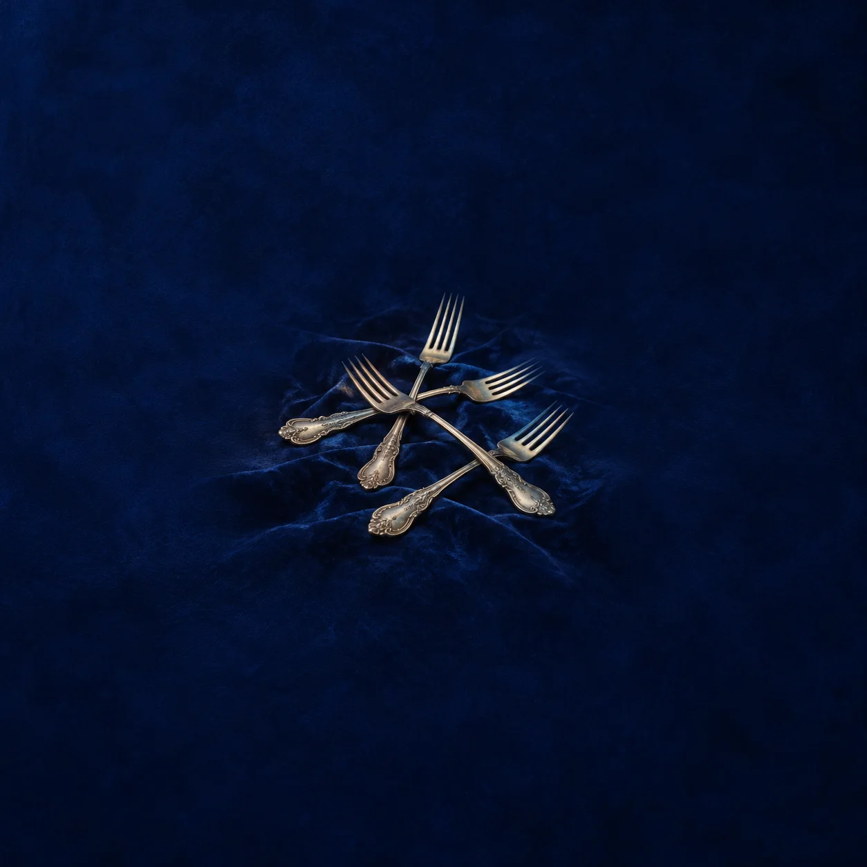 Painterly crossed silver forks on folds of royal blue velvet.