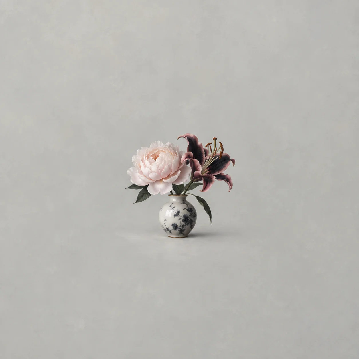A pale peony and a dark lily stand together in a small porcelain vase against a pale grey background.