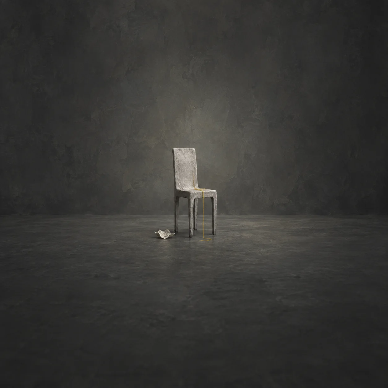 A lone grey chair on a charcoal floor with a crumpled paper scrap and yellow thread draped from its seat.