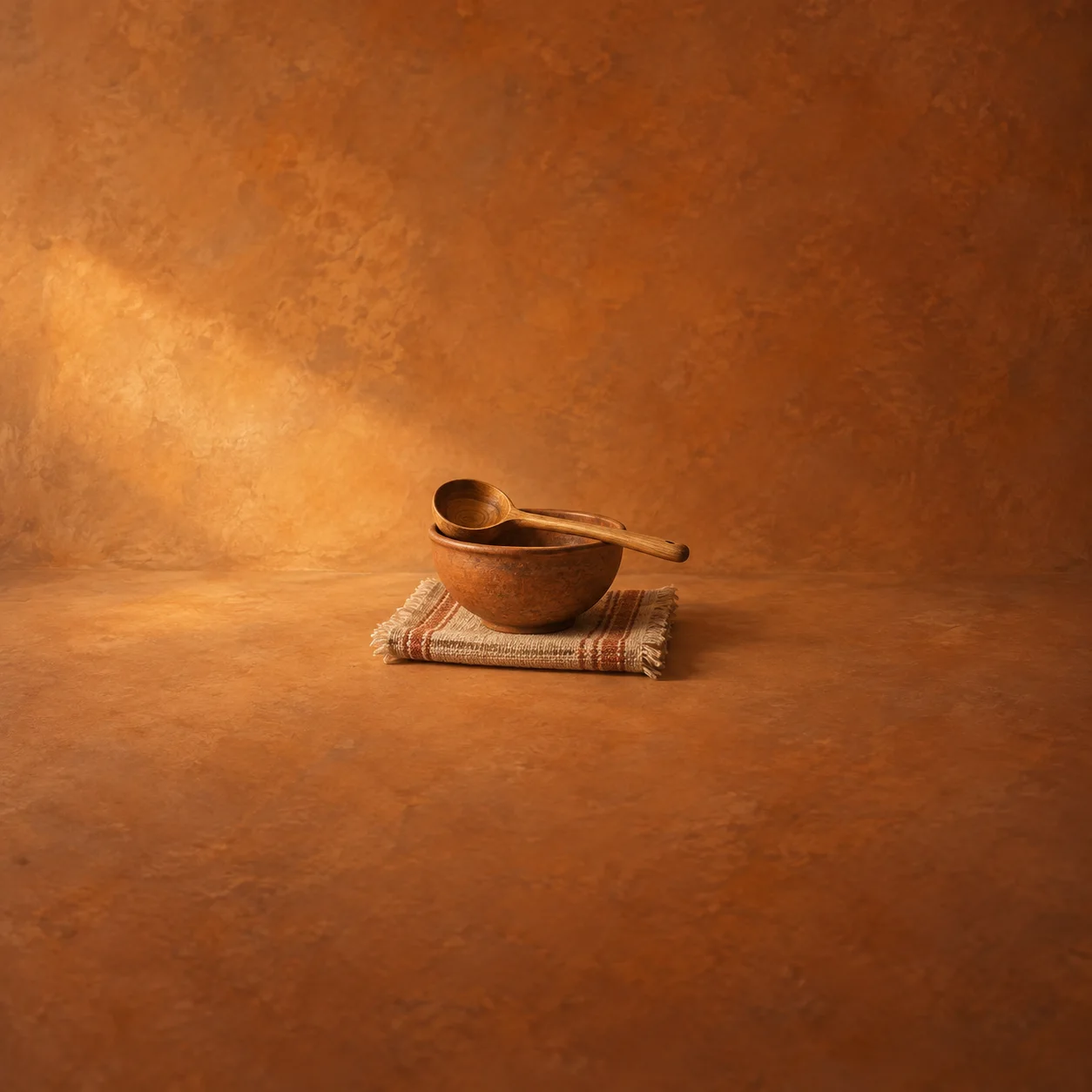 Painterly wooden ladle across a clay bowl on folded woven cloth in warm amber light.