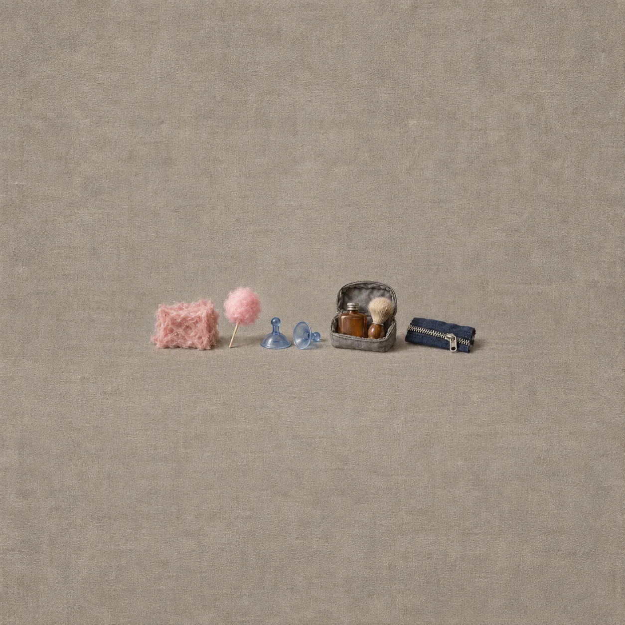 Pink fibre insulation and candy, two blue suction cups, a shaving pouch with brown flask and brush, and a silver zipper on navy cloth form a low row.