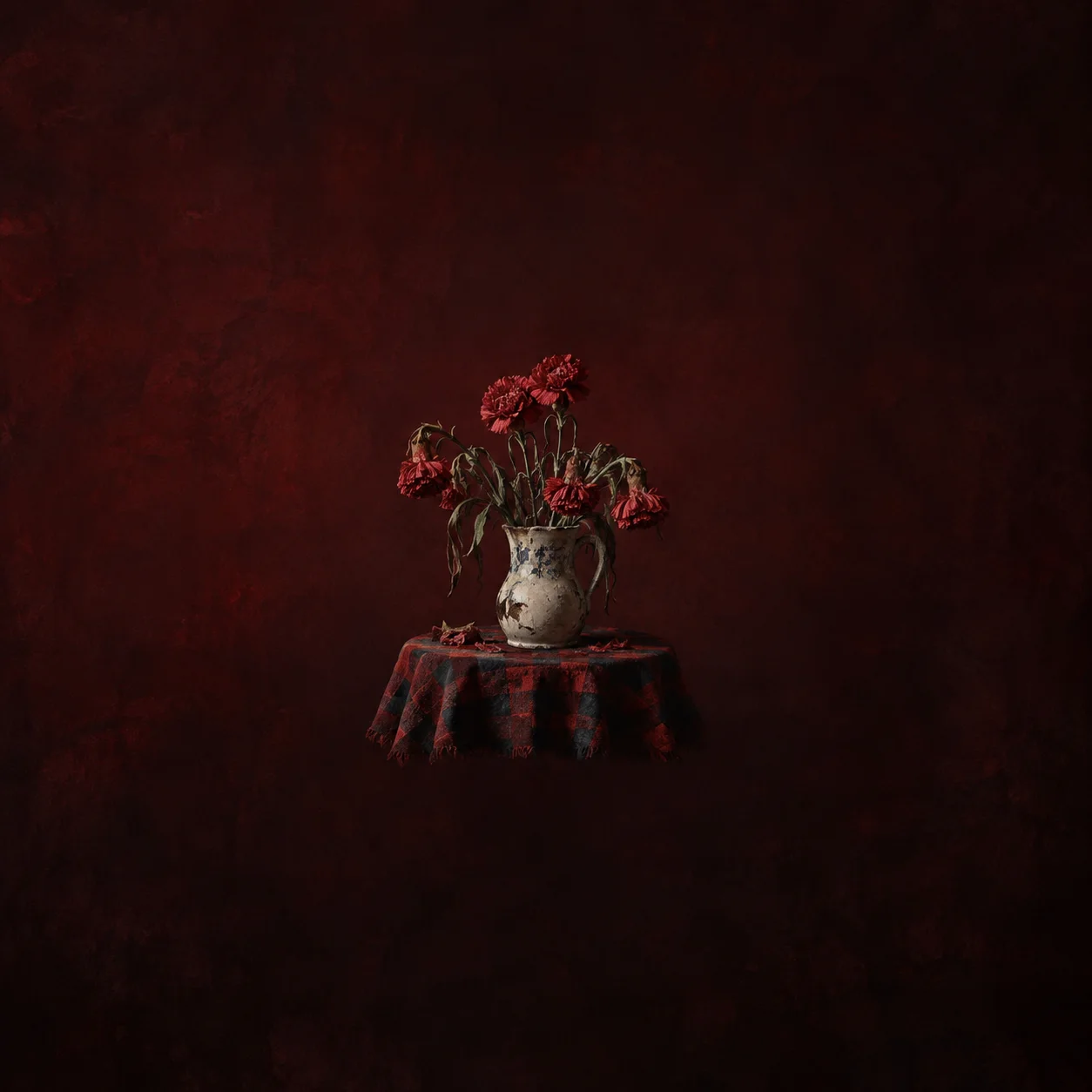 Wilted red flowers stand in a chipped pale vase on a red-and-black checked cloth.