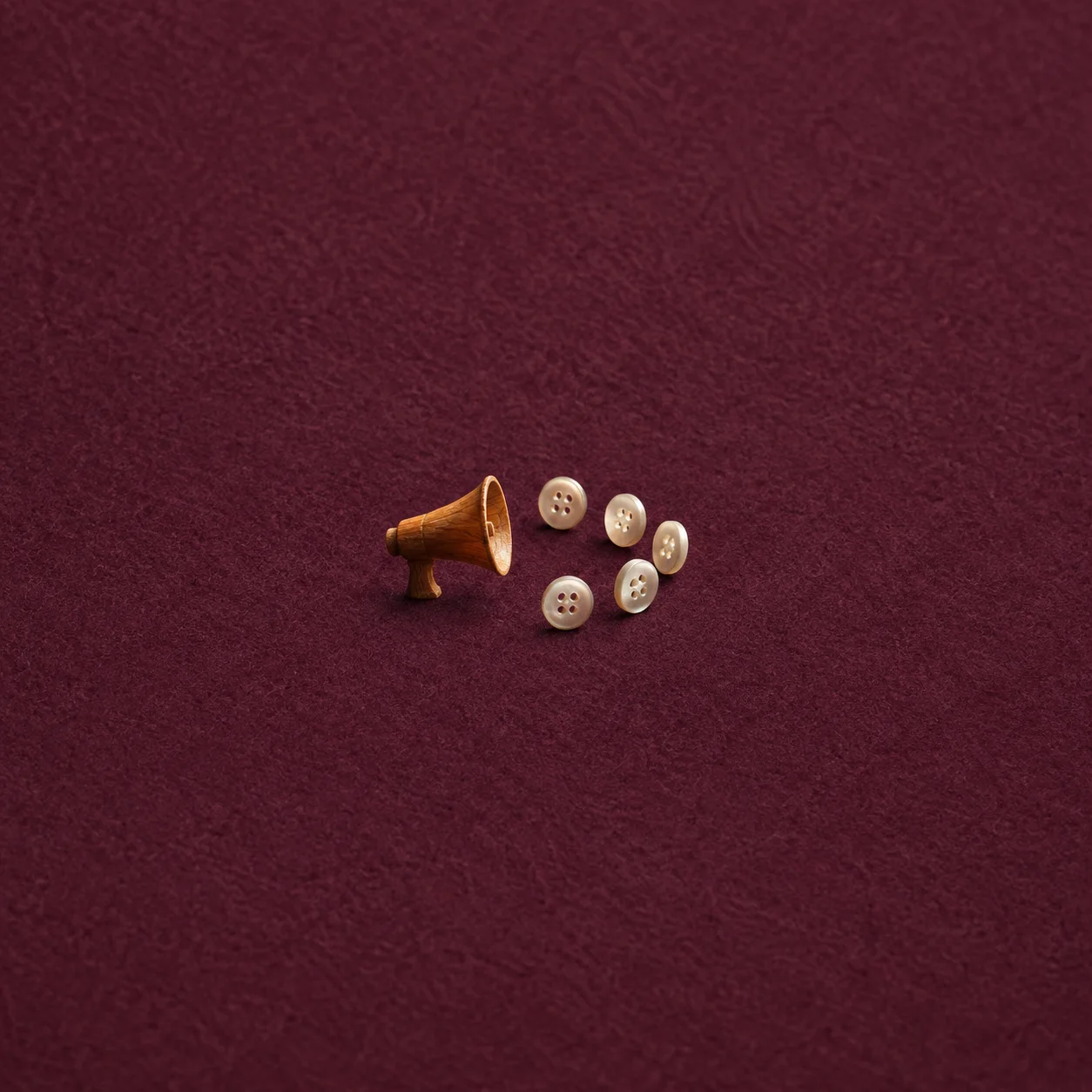 A small golden megaphone faces five pale buttons on burgundy fabric.
