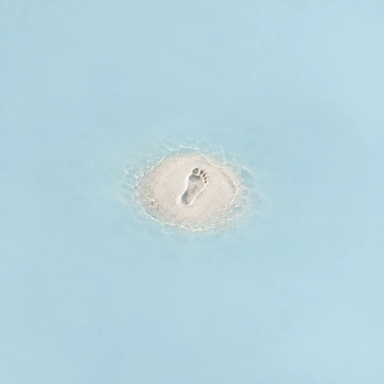 One fresh footprint in a small smooth patch of fine white sand, surrounded by pale blue.