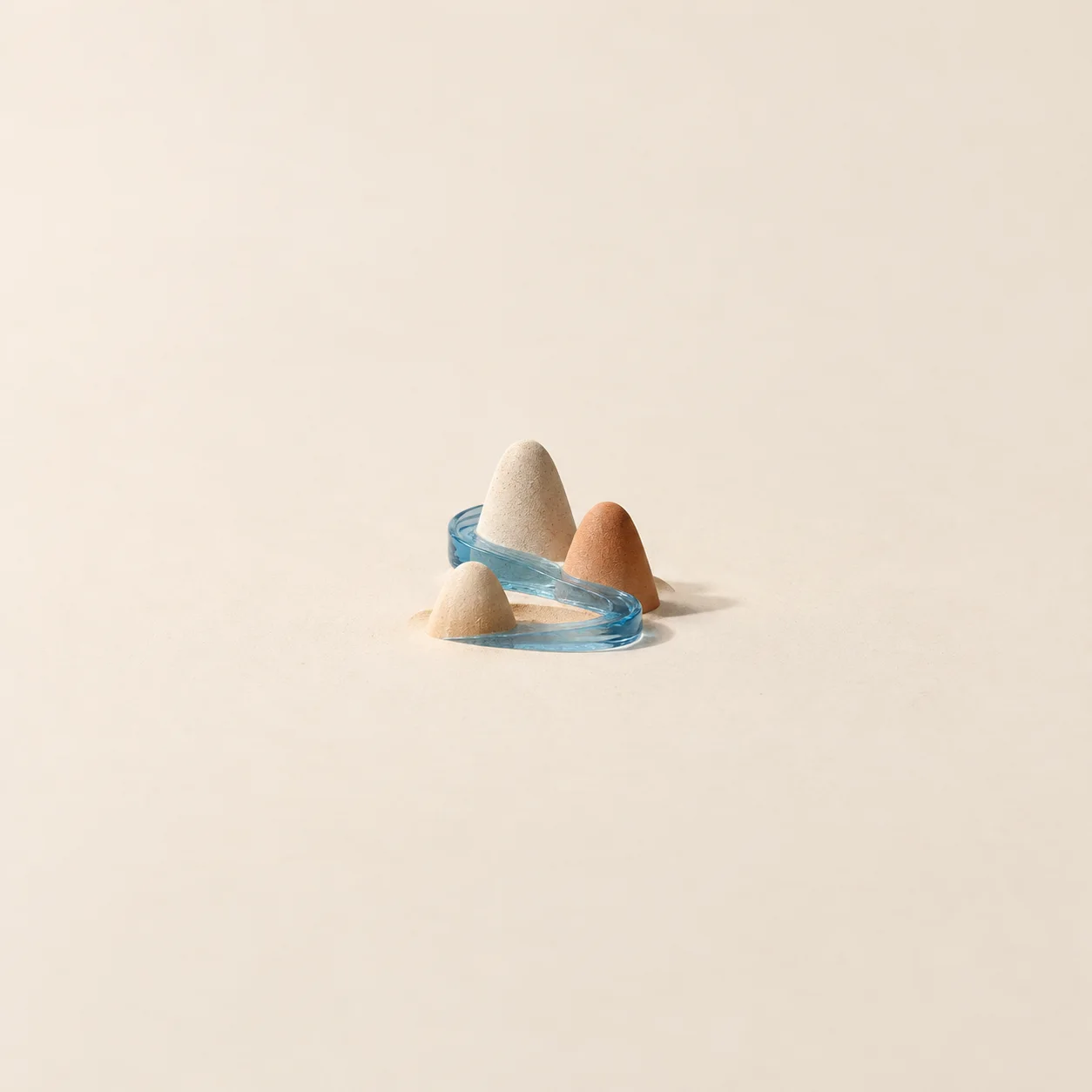 A translucent blue ribbon winding around three small rounded clay hills on a pale surface.