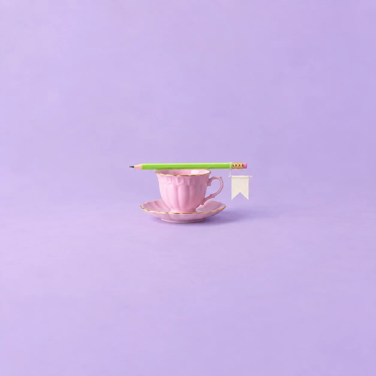 A lime-green pencil resting across a pink teacup and saucer, with a small white flag hanging from one end against a lavender background.