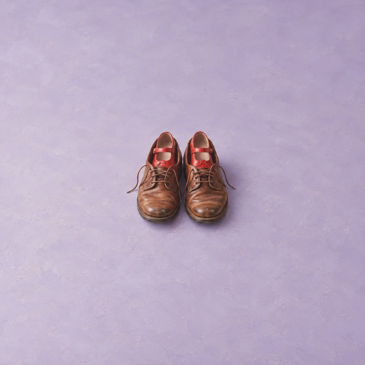 A worn brown pair of leather shoes with a smaller pair of red shoes tucked inside.