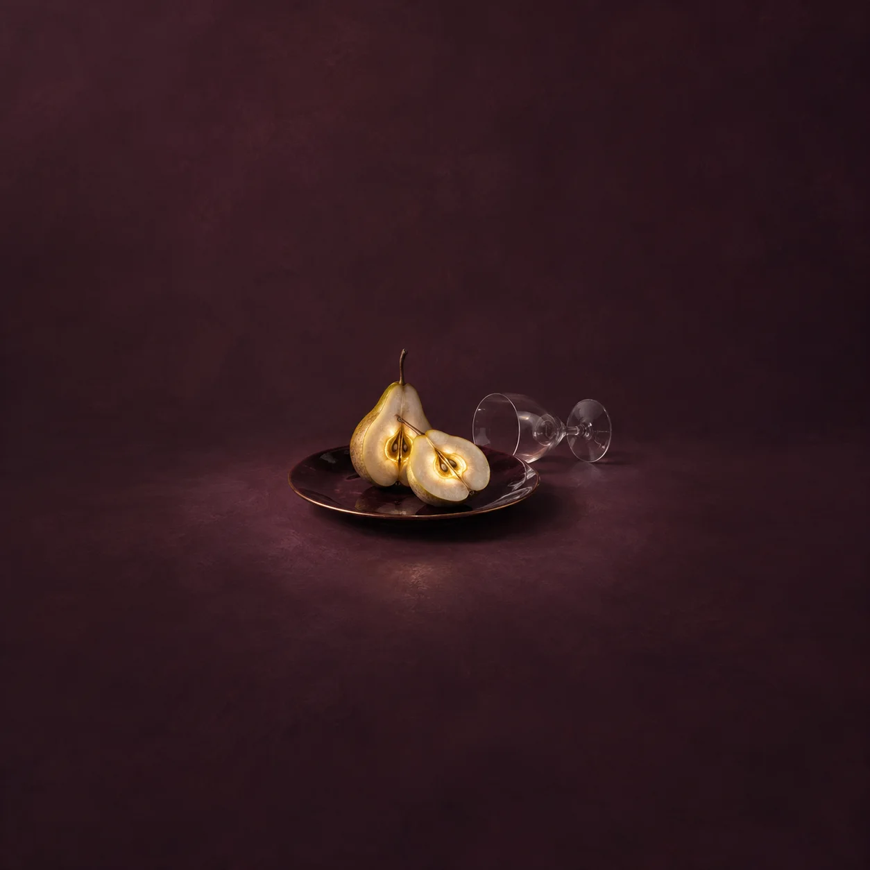 Painterly whole and halved pear on a dark plate beside an overturned wine glass on plum.