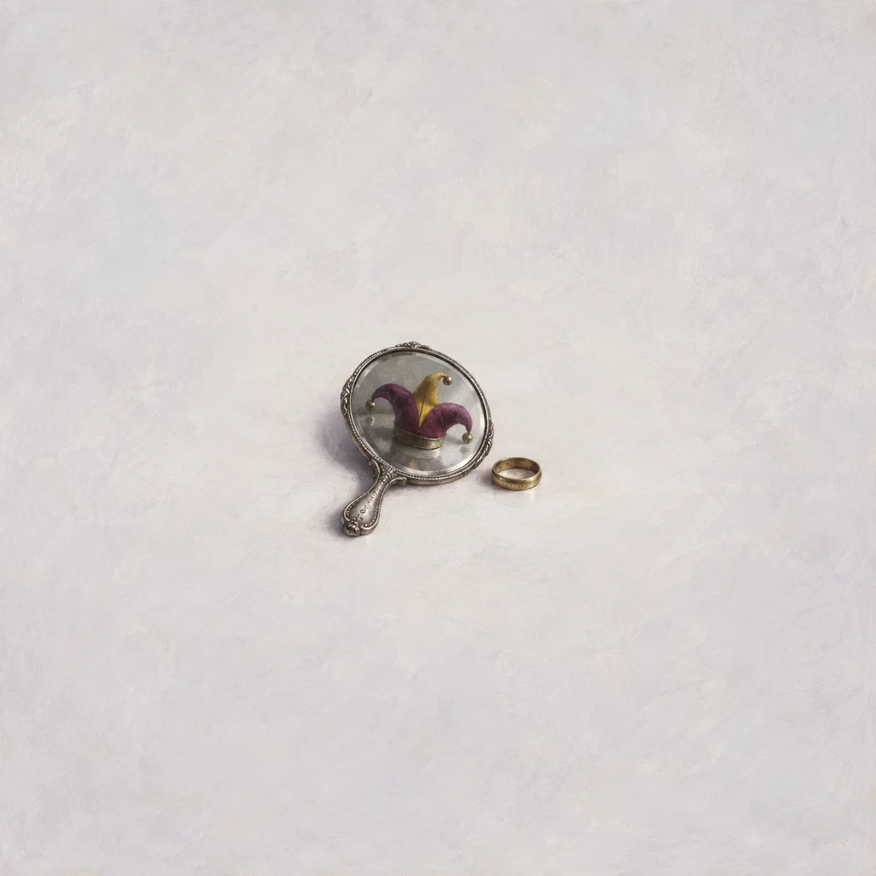 A round hand mirror reflects a small jester’s cap, with a brass ring beside it.