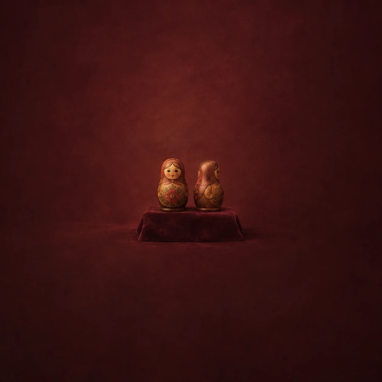 Two painted wooden nesting dolls, one facing forward and one turned away, stand on burgundy velvet.