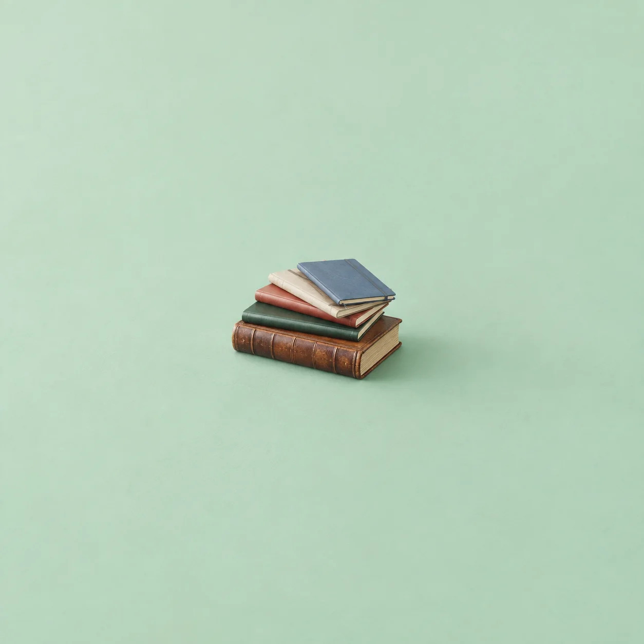 A brown leather volume with a fan of differently colored notebooks tilted over it on a mint surface.