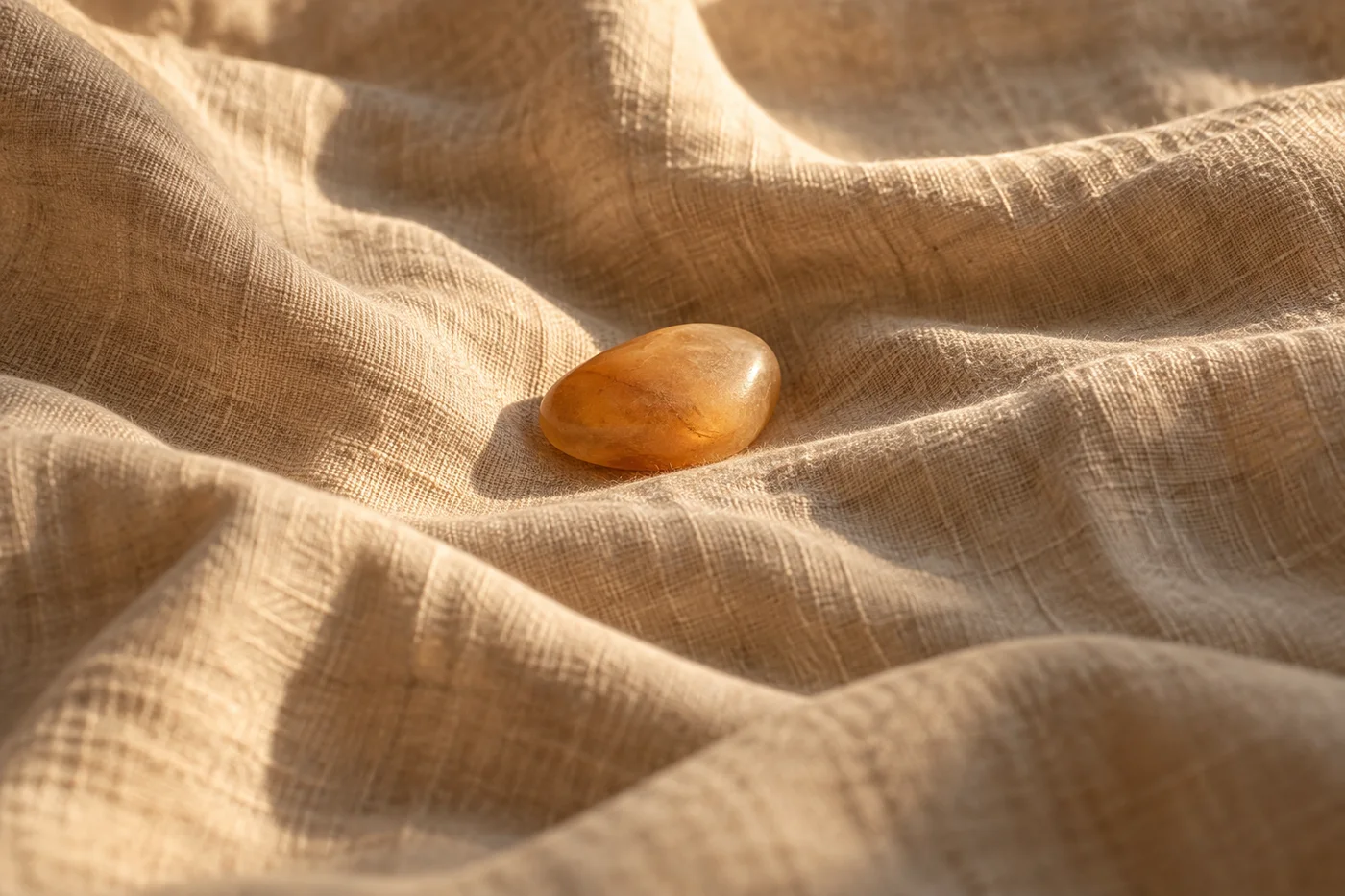 A smooth amber pebble rests in a fold of rumpled oat-coloured linen.