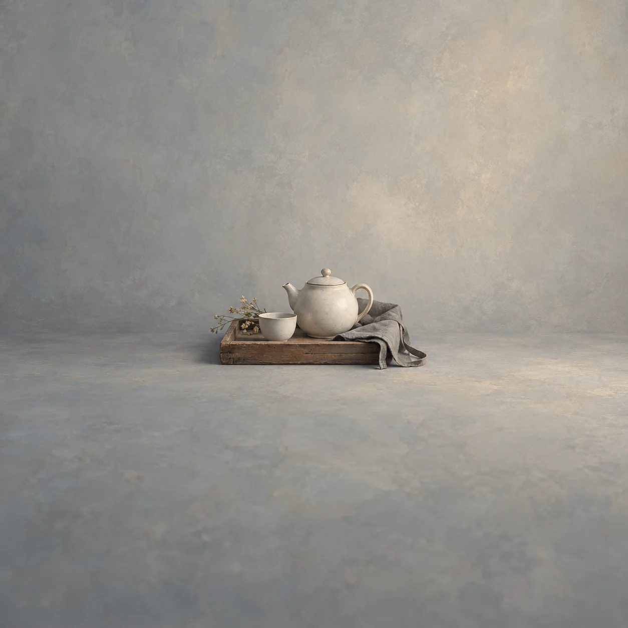 Painterly pale teapot and cup on a wooden tray beside a draped grey cloth.