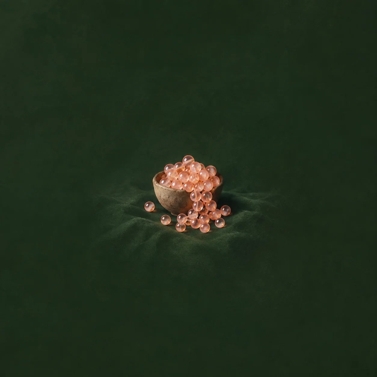 Peach-coloured glass beads spill from a small bowl onto dark-green cloth.