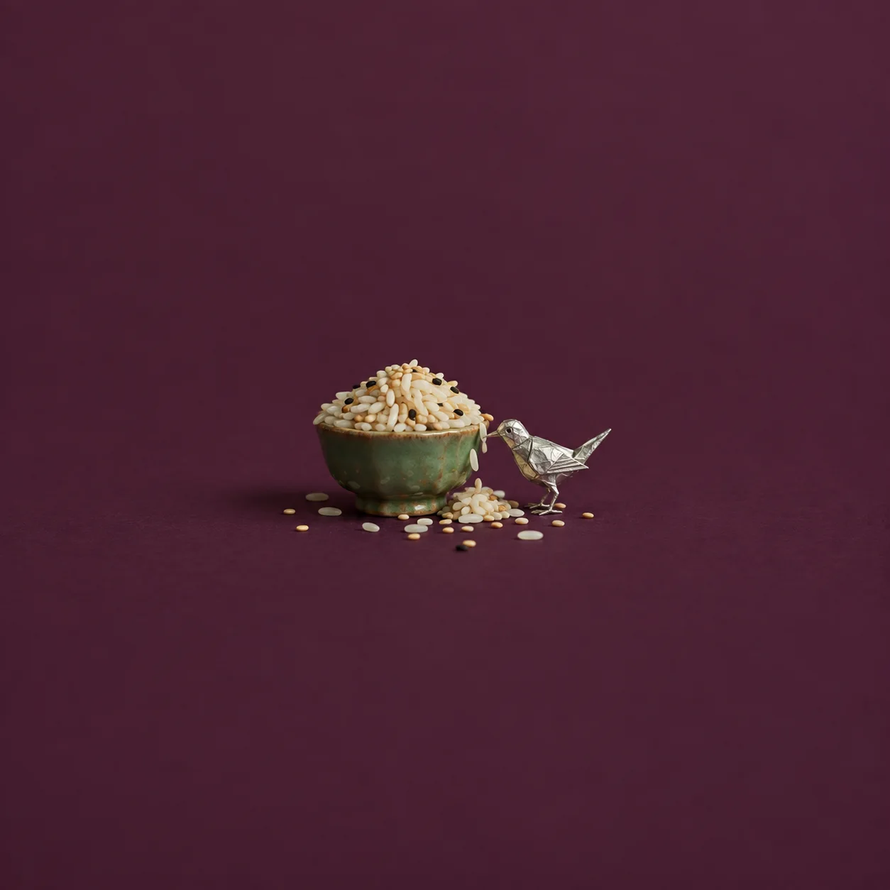 A green bowl piled high with grain beside a small silver bird and scattered grains on a plum background.