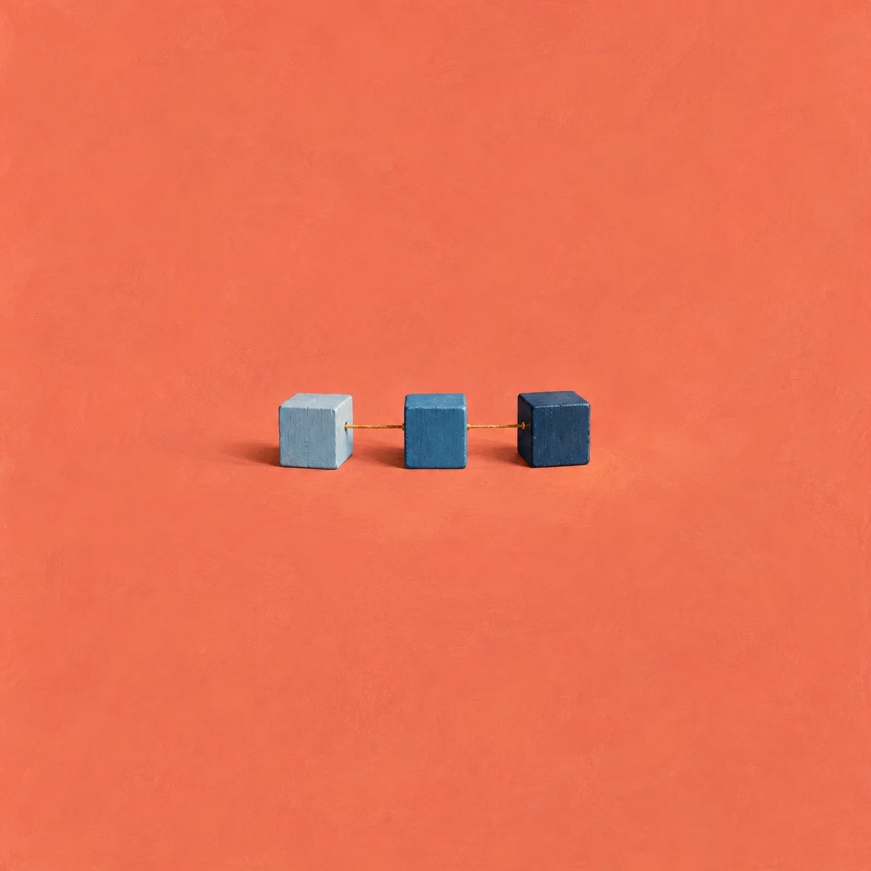 Three blue wooden cubes in a straight row linked by a golden thread on a coral background.
