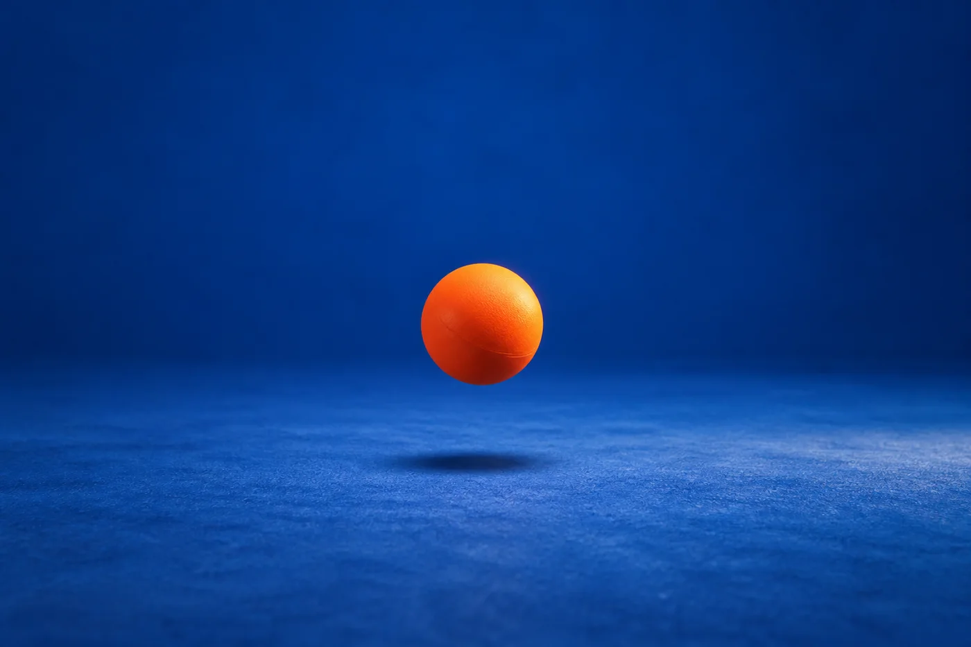 An orange ball hangs above a blue floor, with a soft shadow beneath it.