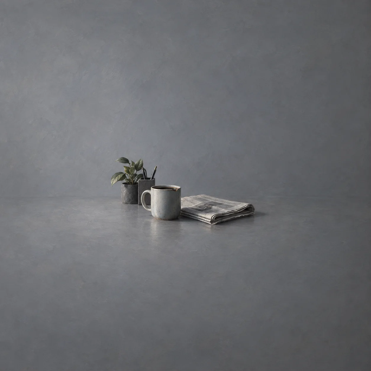 Painterly grey mug beside a folded newspaper and small potted plant.