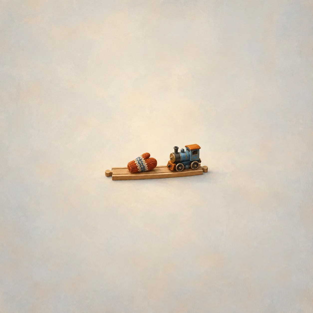 A small toy locomotive facing an orange knitted mitten on a short wooden track.