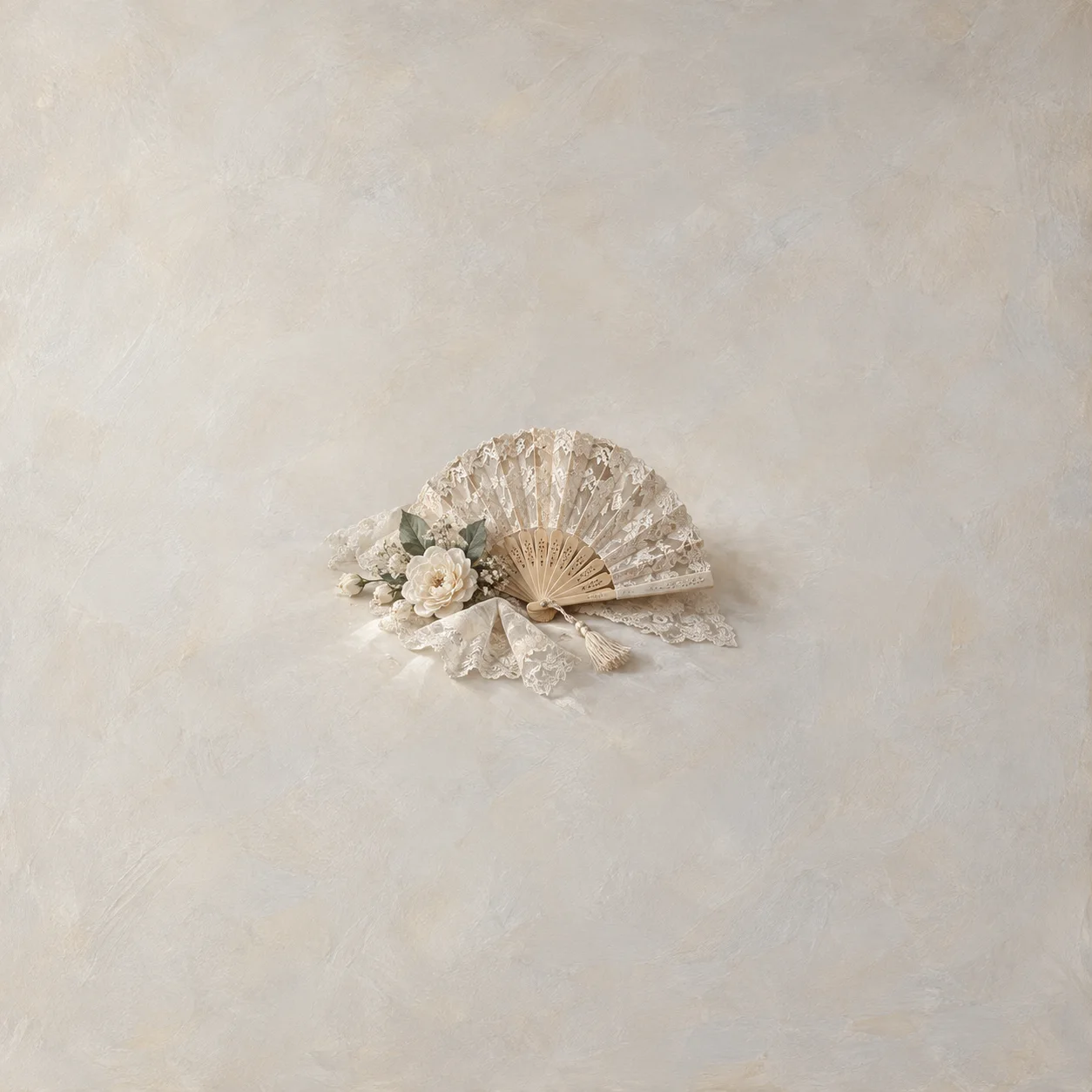 An open ivory lace fan rests beside pale flowers and lace fabric in soft light.