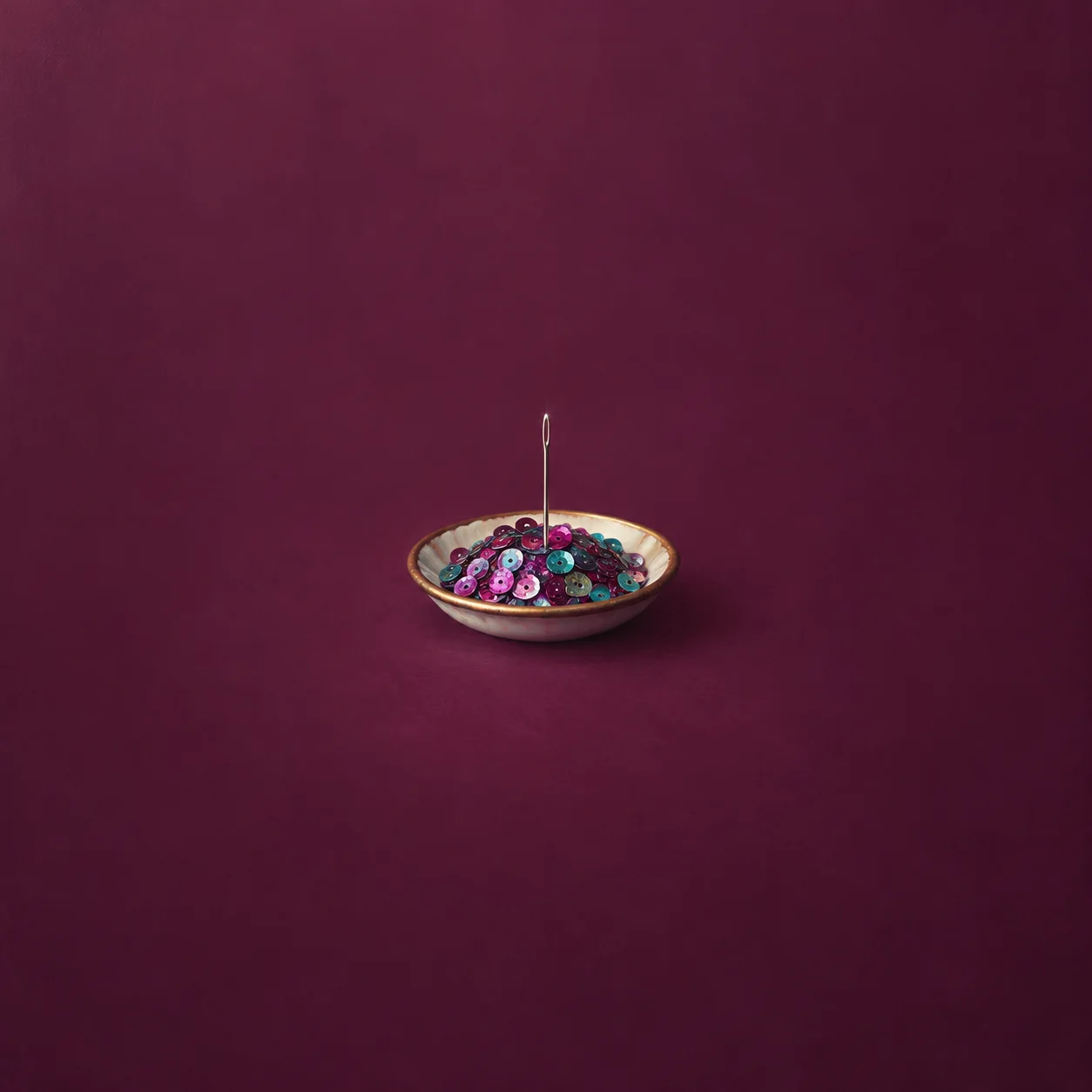 A silver needle stands upright among colourful sequins in a small dish against a burgundy background.