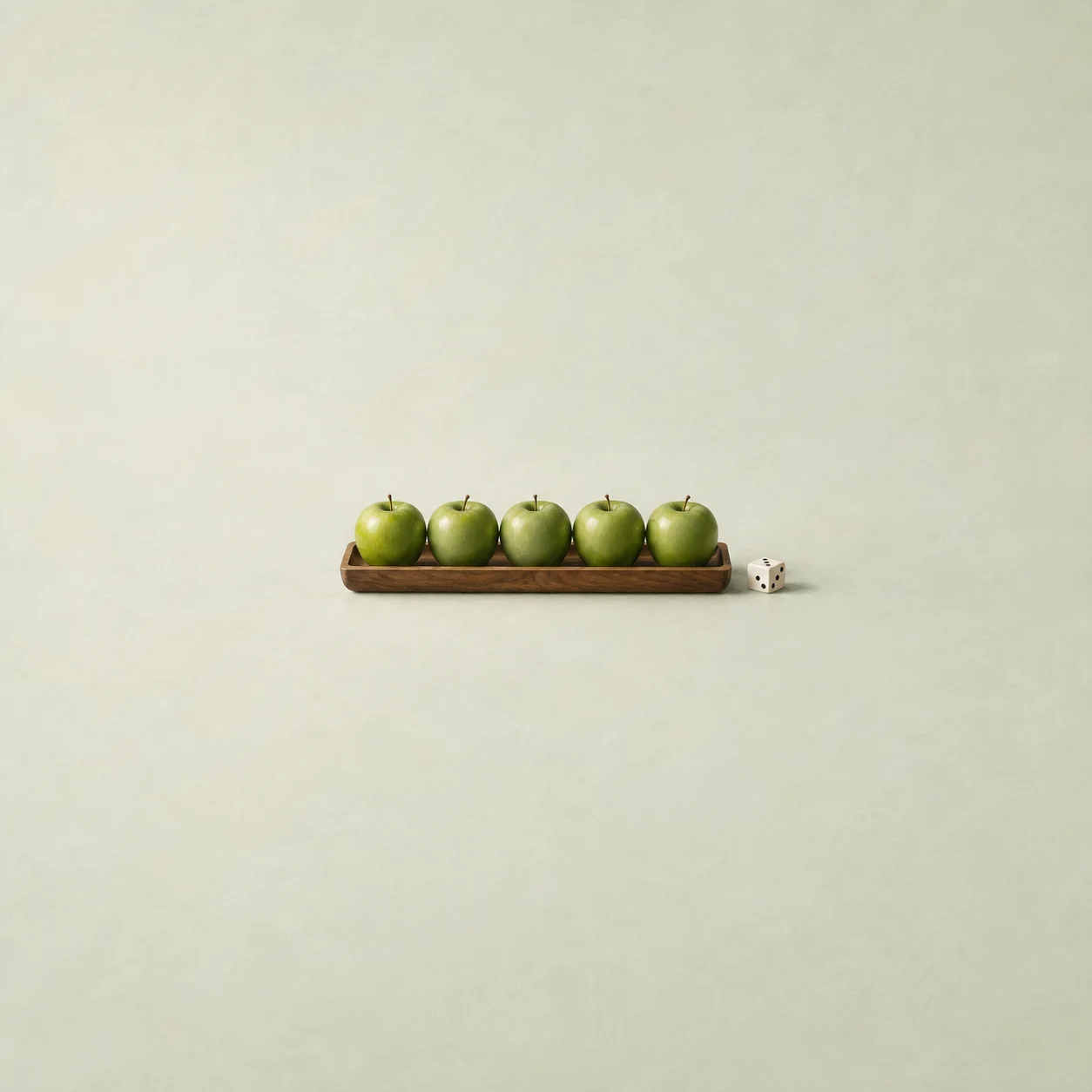 Five green apples lined up on a wooden tray with a white die beside it against a pale green background.