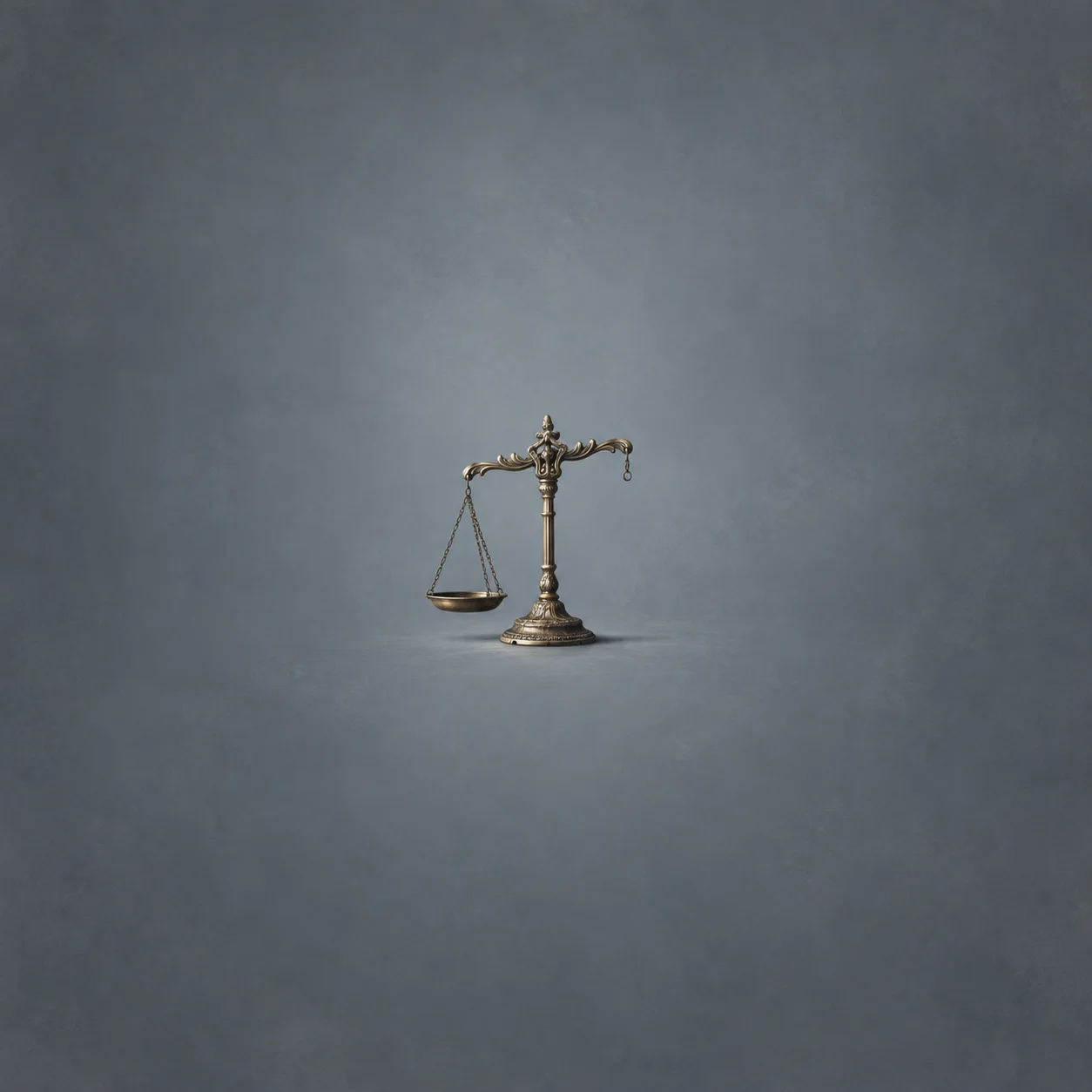 An ornate brass balance scale stands with one hanging pan and an empty hook on the opposite arm against a cool grey background.