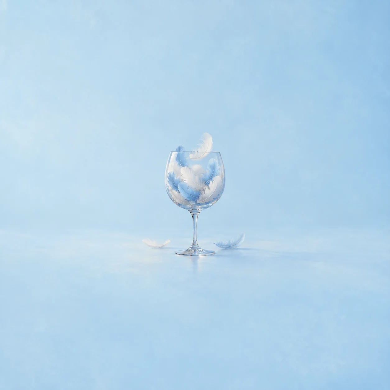 A clear stemmed wine glass holds blue and white feathers, with loose feathers beside it.