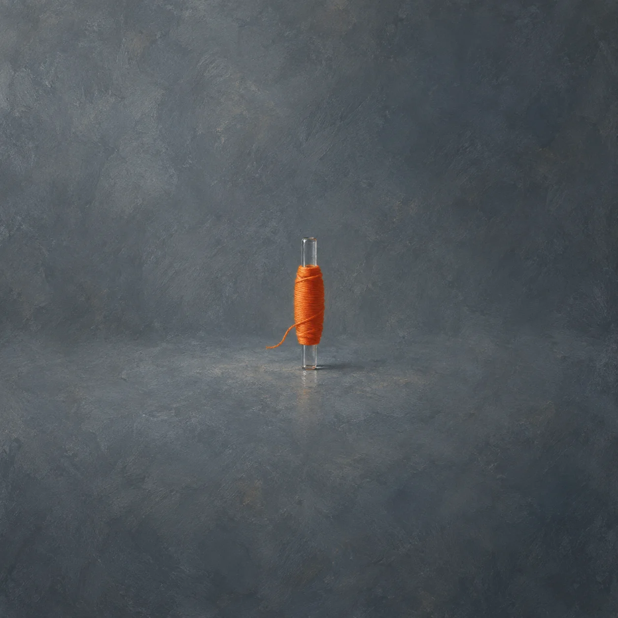 An upright glass rod is wrapped tightly with orange thread against a grey background.