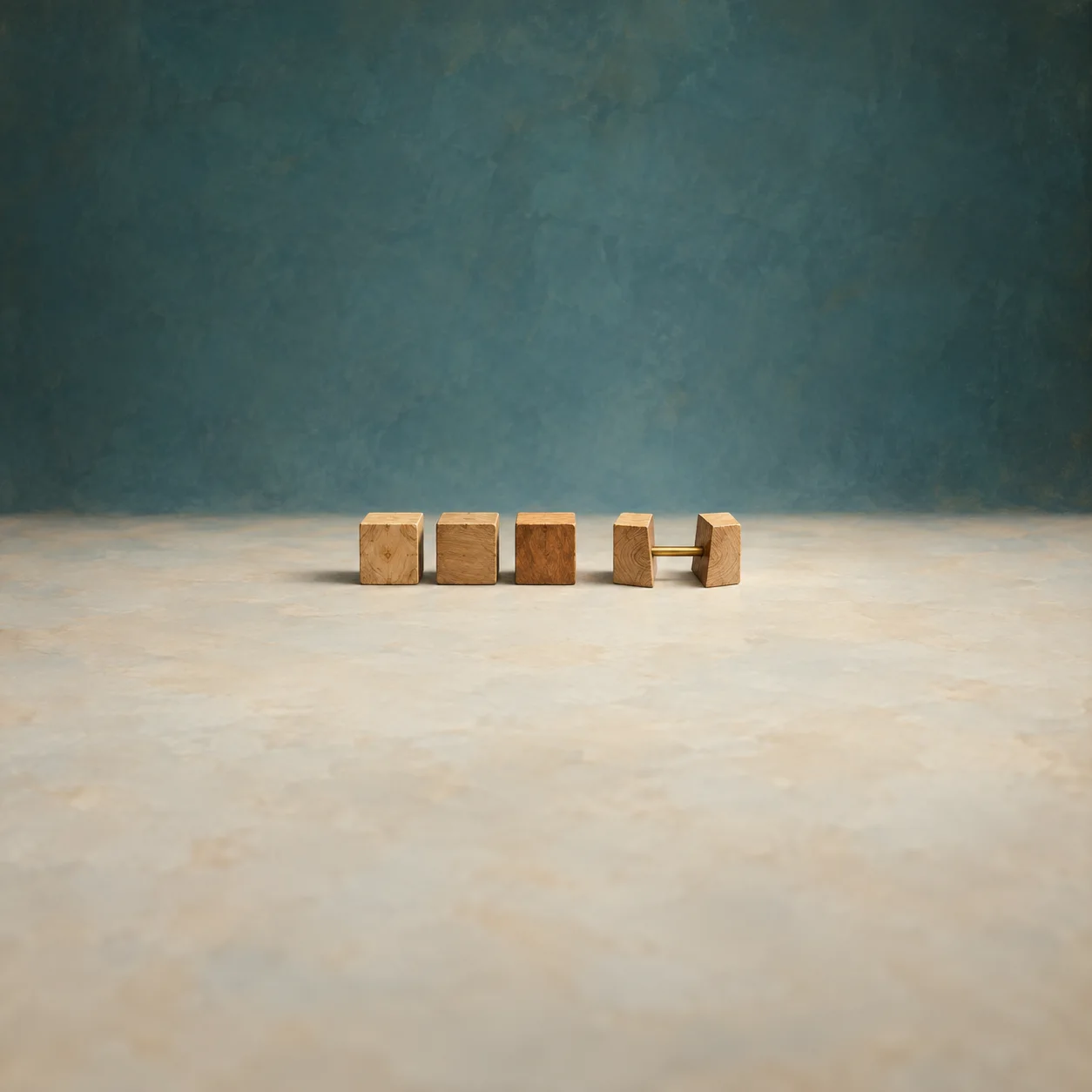 Three wooden blocks stand beside two block halves joined by a brass rod on a pale surface against teal.