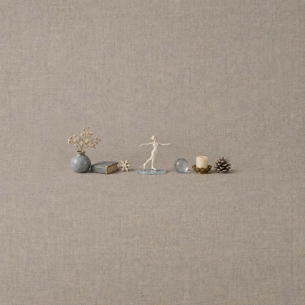 An anonymous ivory porcelain skater in a white one-piece outfit stands on blue glass ice beside a small book, vase, snowflake, orb, candle and pinecone.