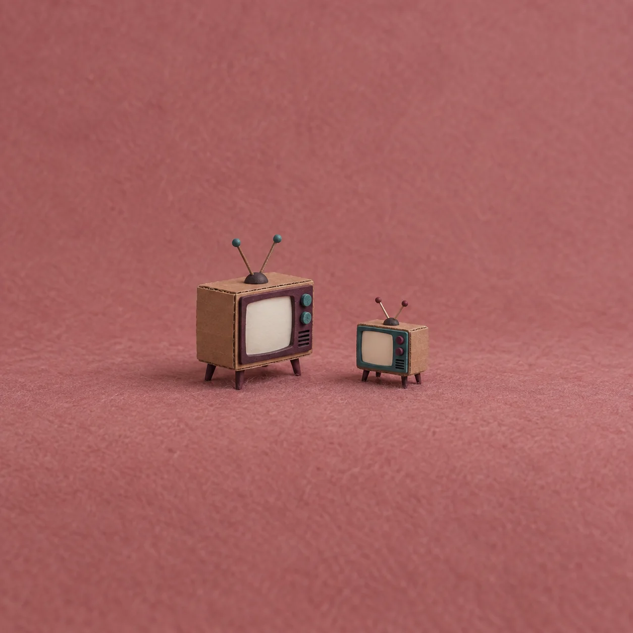 Two small retro televisions with blank pale screens stand side by side against dusty pink.