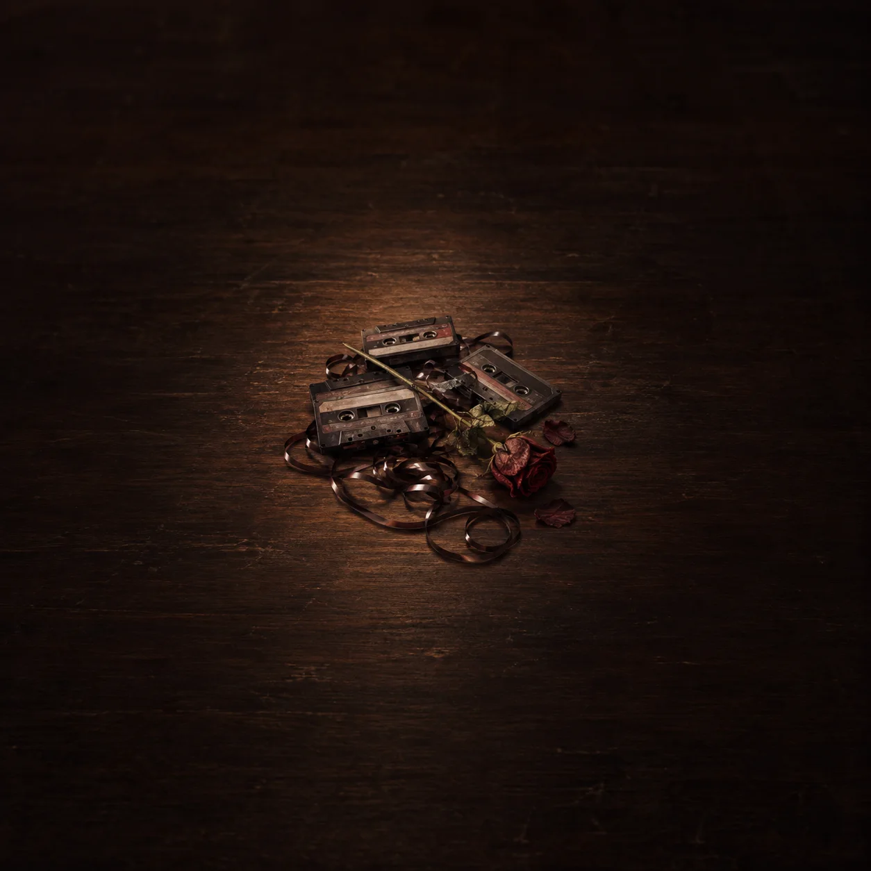Unspooled cassette tapes and a wilted red rose lie on a dark wooden tabletop.