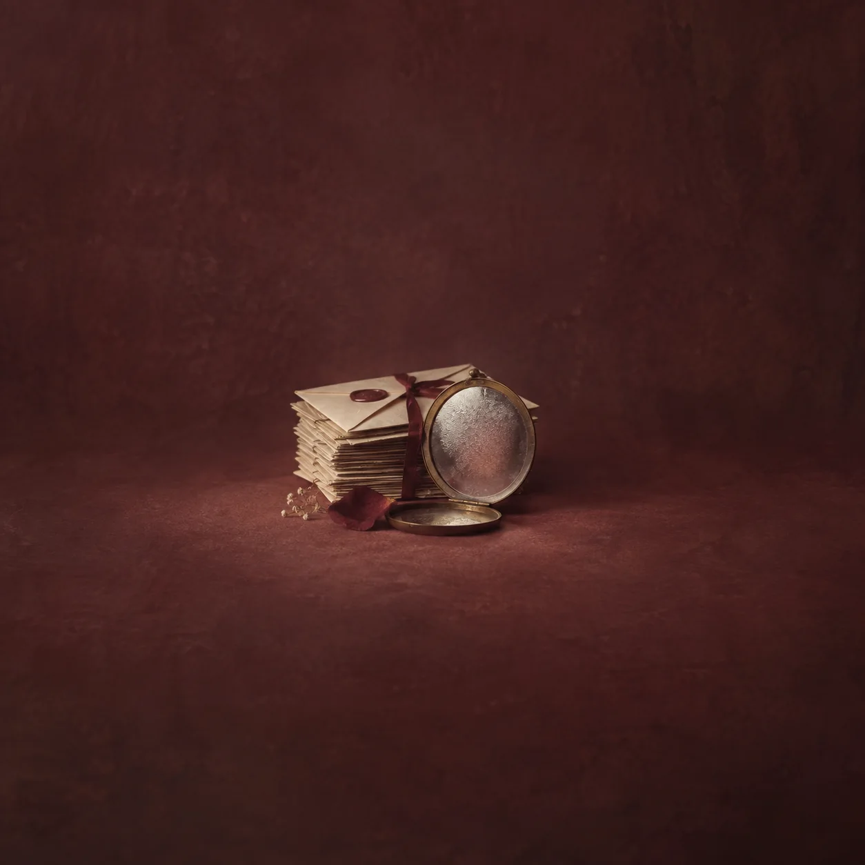 A fogged round mirror rests beside a ribbon-tied stack of sealed letters on burgundy ground.