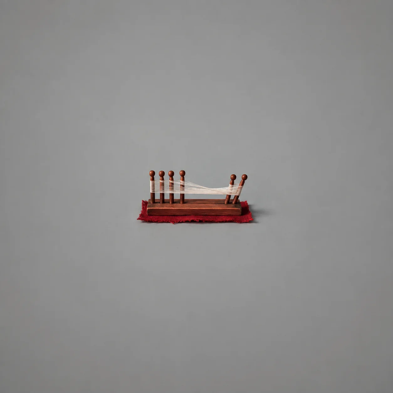 A white thread stretched across small wooden pegs, bending where one peg is pulled out of line.