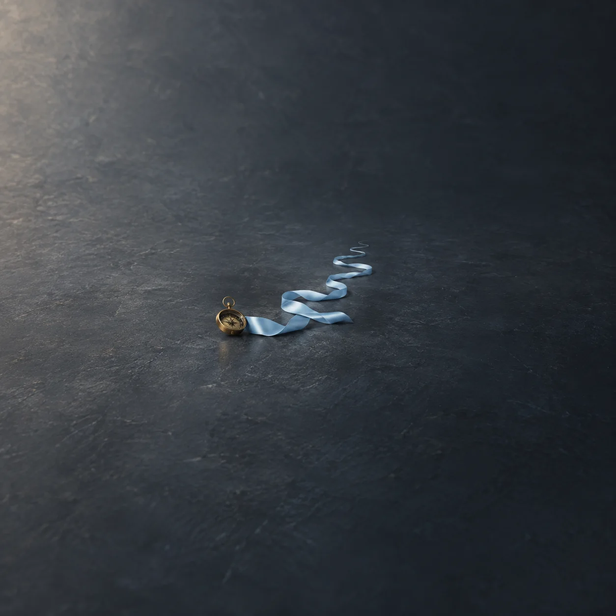 A blue satin ribbon winding away across a dark surface beside a small brass compass.